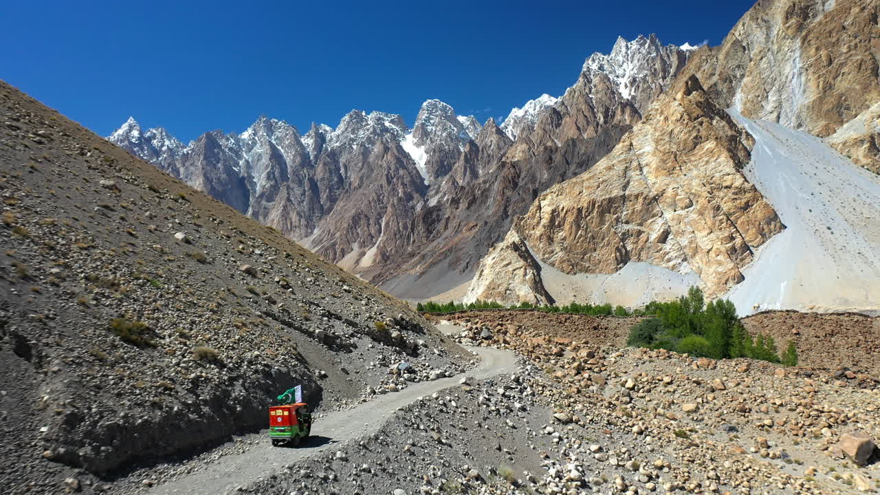 toma cinematográfica de un tuk-tuk en un camino de grava en la autopista karakoram pakistán con los conos passu en la distancia, toma aérea descendente