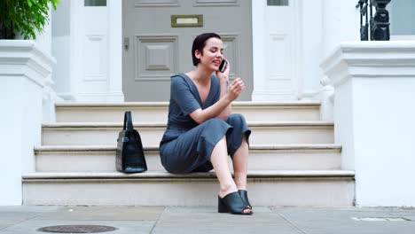 Stylish-Woman-Sitting-On-Steps-Of-Building-Using-Mobile-Phone