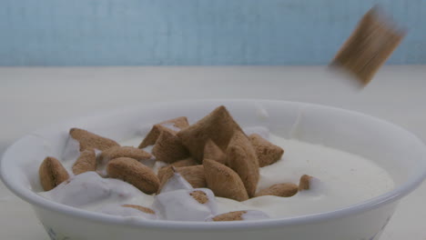 Chocolate-pillows---pads-slide-into-a-bowl-of-creamy-milk-in-slow-motion---a-blue-wooden-background-in-the-background