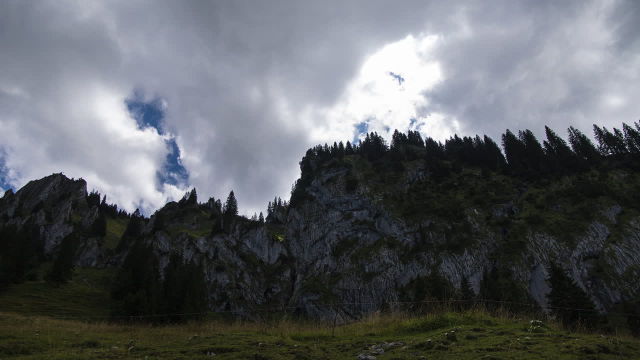 Time-lapse shot of clouds in front of a large rock in the Allgäu Alps in Bavaria, Germany. The sun is occasionally obscured by the clouds.