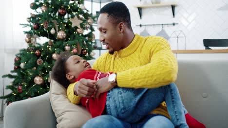 Portrait-Of-Happy-Father-Speaking-And-Playing-With-Little-Kid-While-Sitting-On-Sofa-In-Christmassy-Decorated-Room-Handsome-Loving-Dad-And-Child-Spending-Time-Together-Holidays-Concept