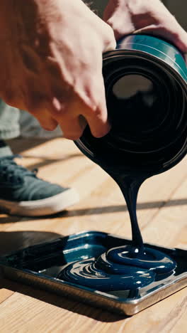 hand pouring dark blue paint into a paint tray