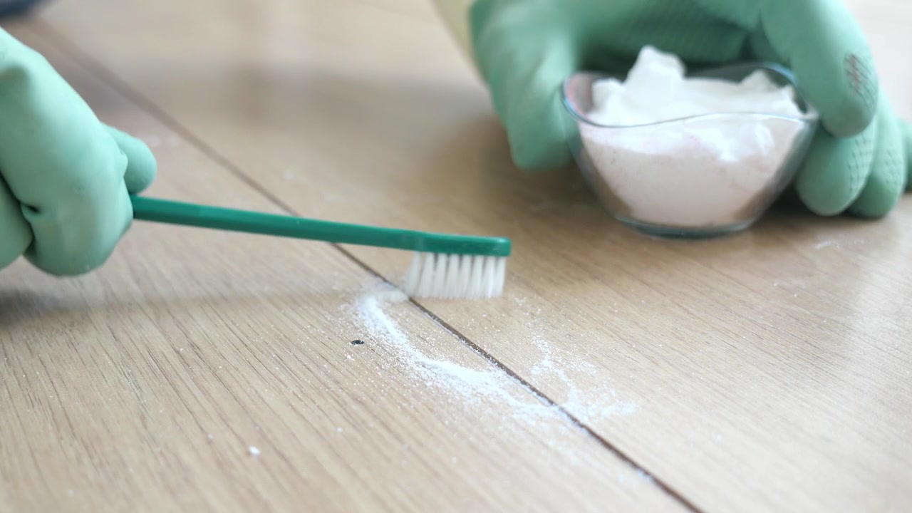Person Cleaning Wooden Floor Grout with Toothbrush and Powder
