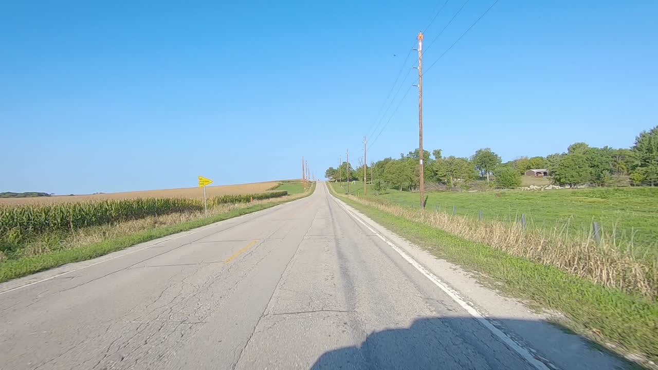 pov는 화창한 초가을날 아이오와 시골에 있는 충분히 성숙하지 않은 옥수수 밭, 목초지, 농장 구내를 지나 다리 위를 운전합니다.