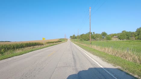 pov driving over a bridge and past not quite mature corn fields, pastures and farmyards in rural iowa on a sunny early autumn day