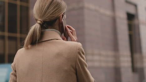 rear view of caucasian charming businesswoman in elegant clothes walking on the street and talking on the phone