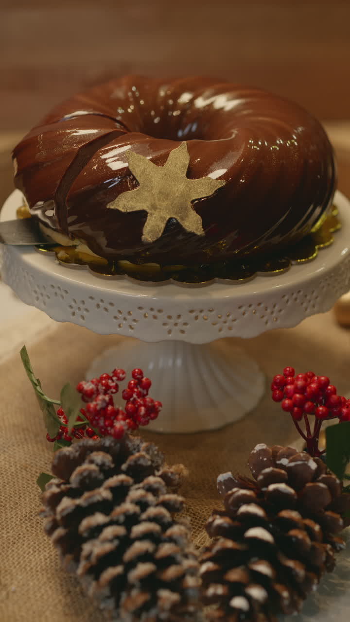 Close-up of an elegant Christmas dessert with glossy chocolate frosting, decorated with a gold star, presented on a pedestal. The clip shows a cut slice highlighting the cake's soft, festive texture
