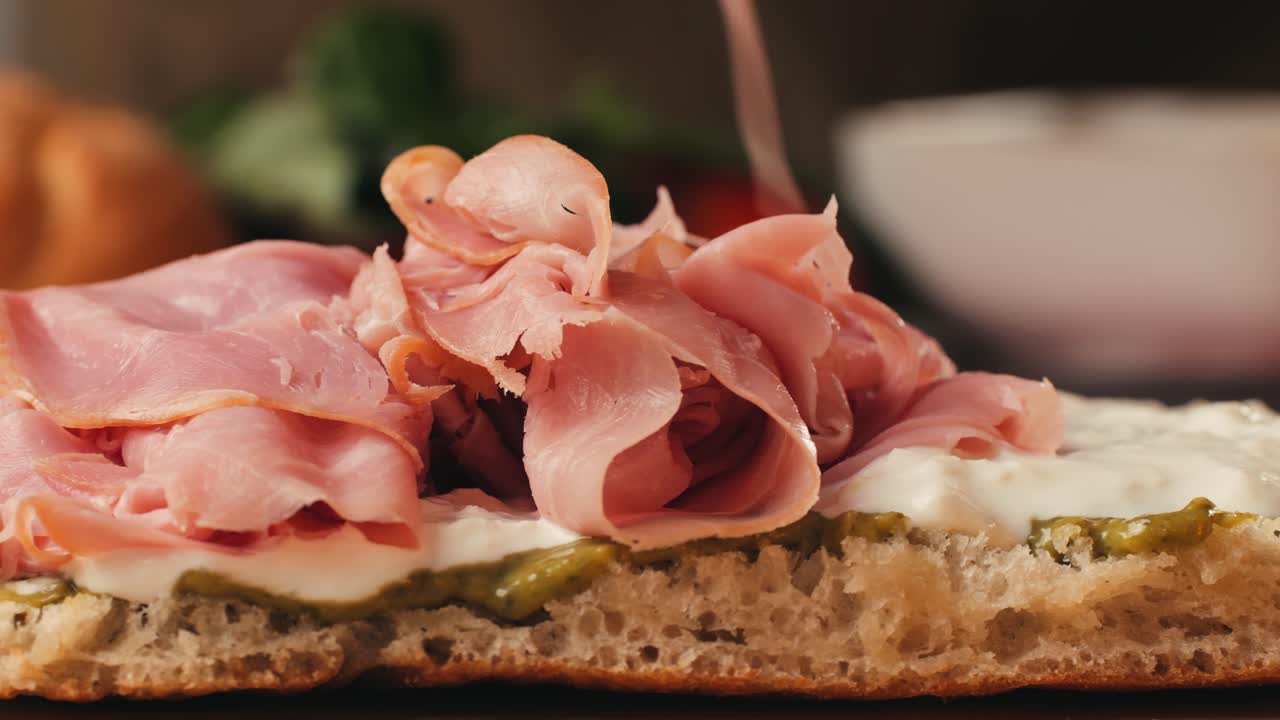 Mortadella ham sandwich, Traditional italian focaccia filled with thin pesto slices of mortadella, served by chef man in cafe restaurant. Macro of traditional italian spanish tapas antipasti.
