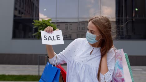 Chica-Con-Máscara-Protectora-Con-Bolsas-De-Compras-Mostrando-La-Inscripción-De-La-Palabra-De-Venta-Durante-La-Pandemia-De-Covid-19