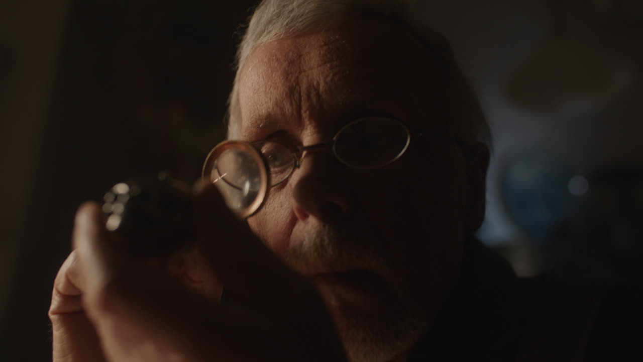 Older passionate man evaluates an old silver skull watch in his office at night