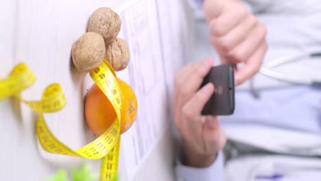 video vertical del médico nutricionista con teléfono inteligente y nueces, naranja y cinta métrica en la mesa