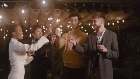 group of four multiethnic friends drinking champagne and having fun with sparklers at new year's eve party