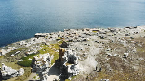 Drone-view-of-two-people-walking-towards-a-sea-stacks,-Gotland,-Sweden