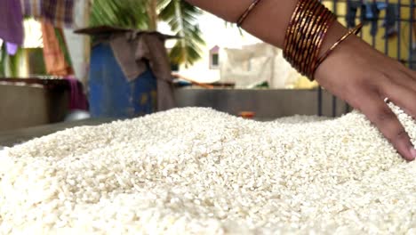 a hand of a girl or lady arranging and running fingers through rice pellets to dry the content