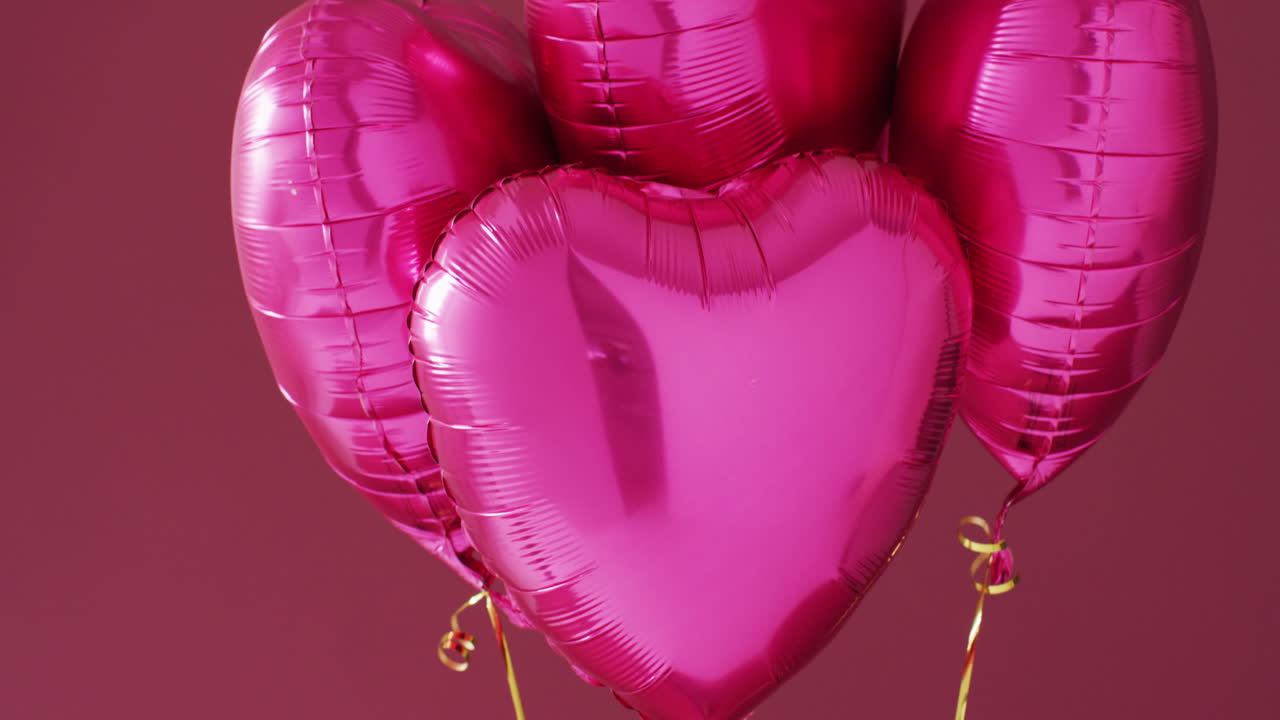 Video de cuatro globos brillantes de color rosa en forma de corazón flotando sobre un fondo rosa.