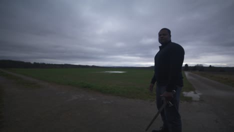 Modern-Black-Swordsman-Warrior-Awaiting-Battle-Opponent-in-Open-Field-Under-Grey-Sky,-Europe,-4K-|-Muscular,-Intimidating,-Shadow,-Figure,-Blurry,-Dark-Clothes,-Powerful,-Stance,-Excited,-Swing-Stance