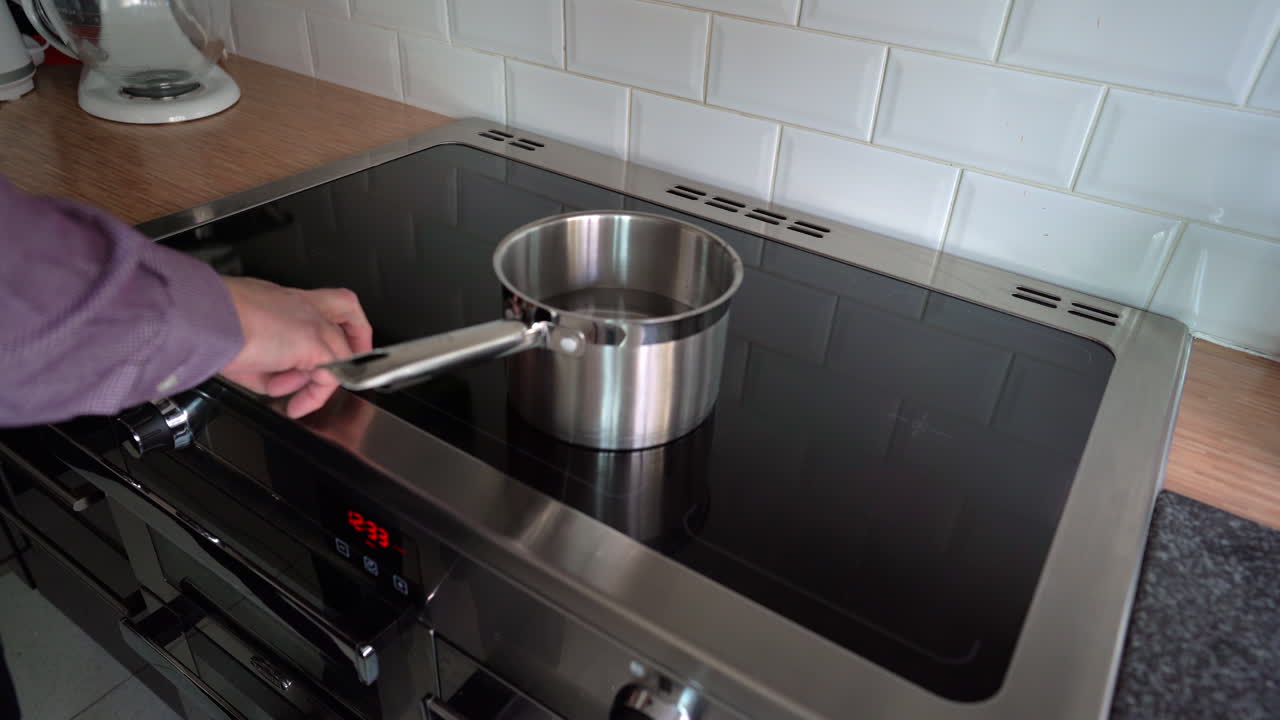 Induction hob man adjusts heat setting for boiling water in a pot on the induction plate
