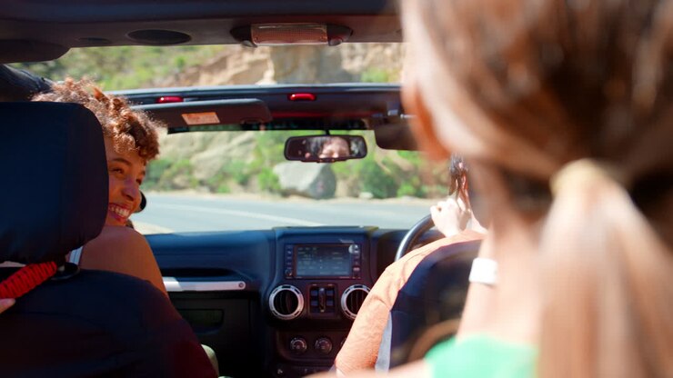 Gruppo di amiche che ridono e si divertono in un'auto decappottabile durante un viaggio on the road