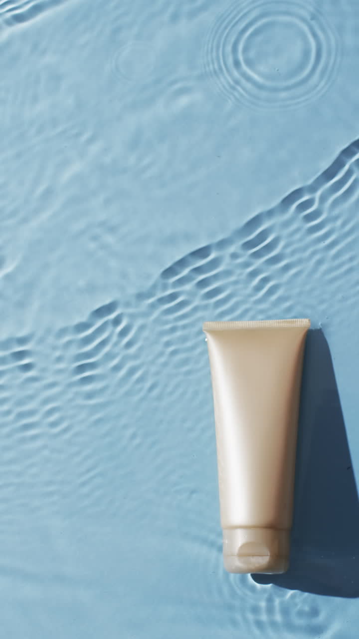 Vertical video of beauty product tube in water with copy space on blue background