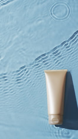 vertical video of beauty product tube in water with copy space on blue background