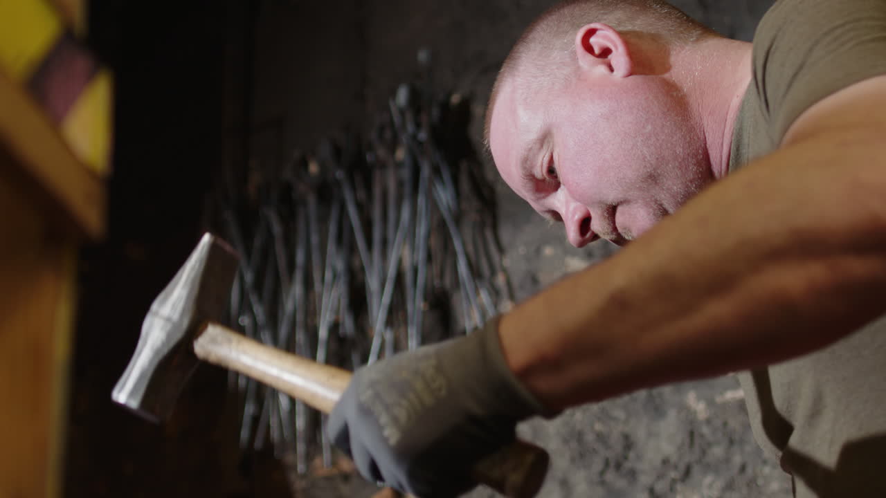 Focused blacksmith in workshop strikes red hot metal on anvil with hammer, slomo
