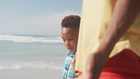 african american son holding his father's hand while walking on the beach