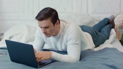 Concentrated-man-laying-with-computer-on-bed-in-luxury-house.