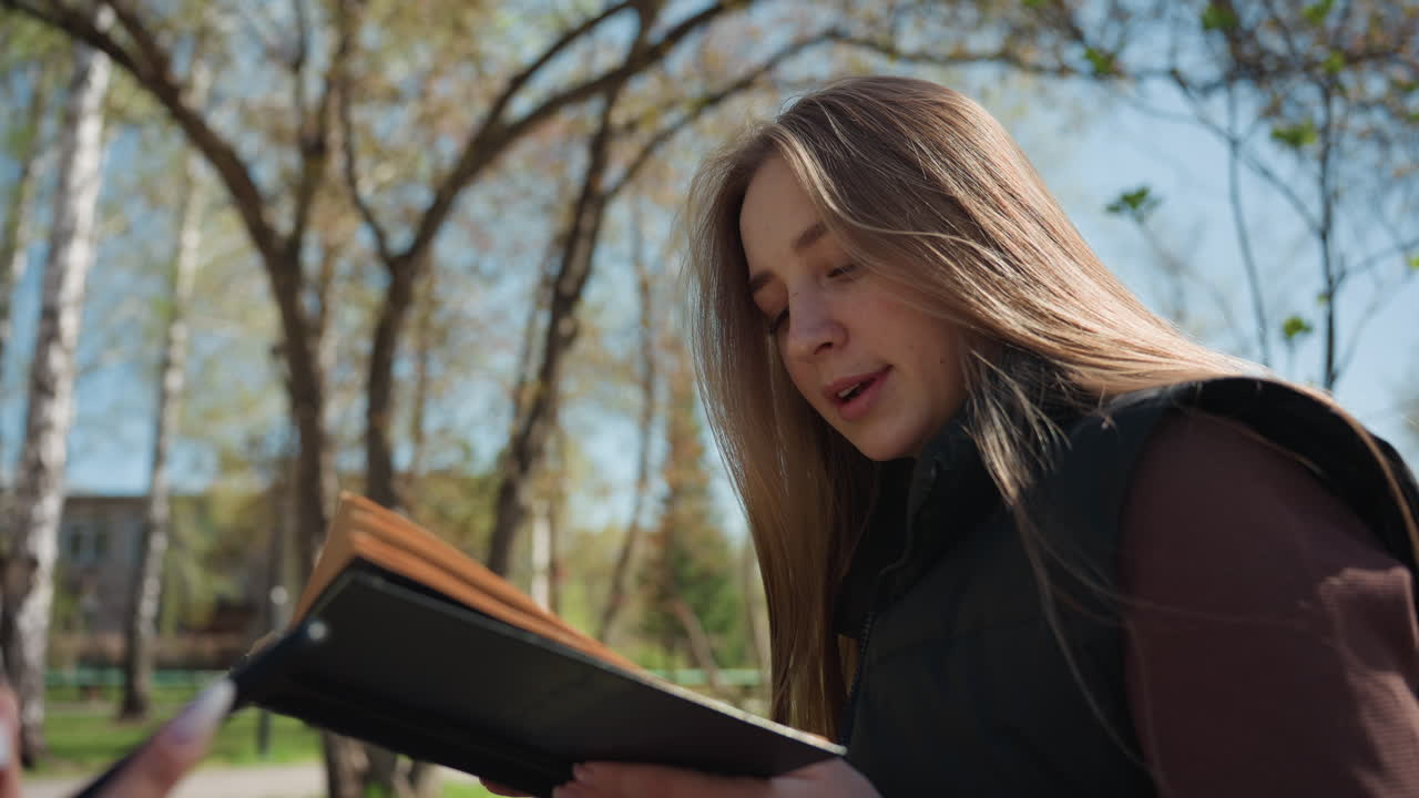 Un poeta lee al aire libre y recita poesía a la luz del sol; un poeta interpreta con pasión bajo ramas frondosas; un poeta versátil ofrece poesía expresiva en un entorno al aire libre iluminado por el sol y rodeado de árboles.