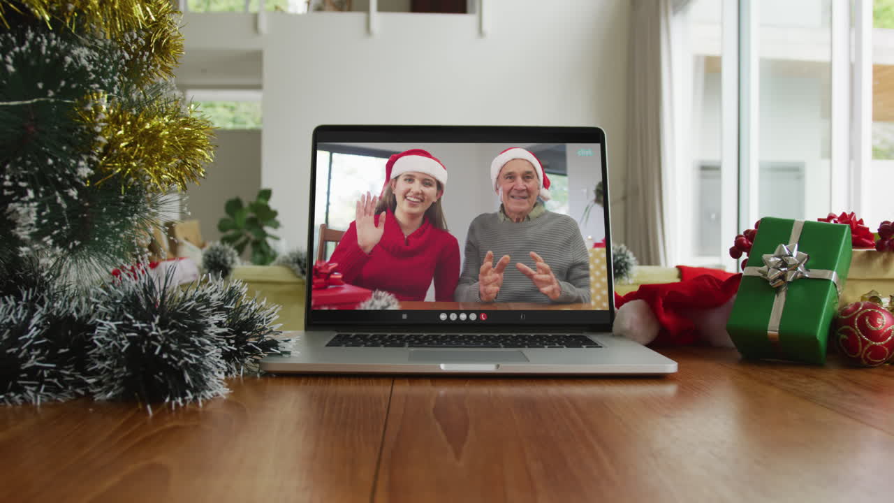 padre caucásico sonriente con su hija usando sombreros de santa en una videollamada de navidad en una computadora portátil