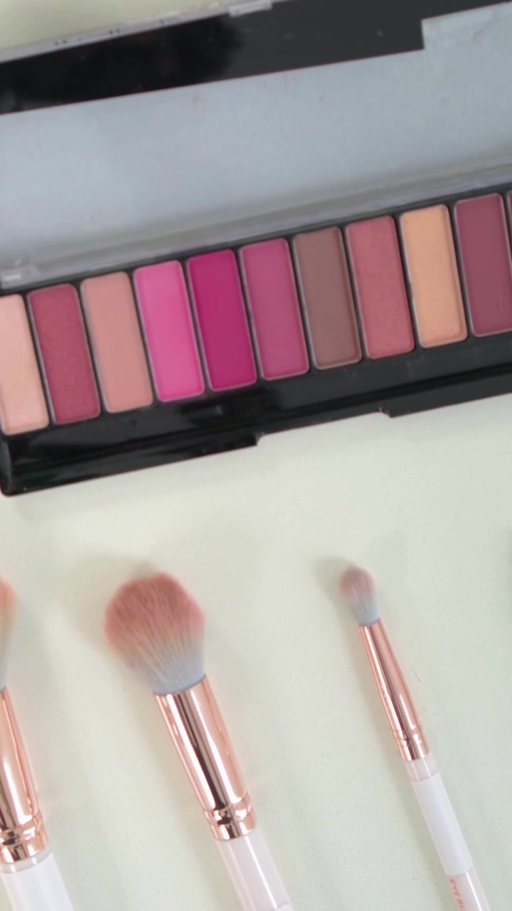 Vertical video: Panning camera revealing brushes, palette and lipstick on pale table for display