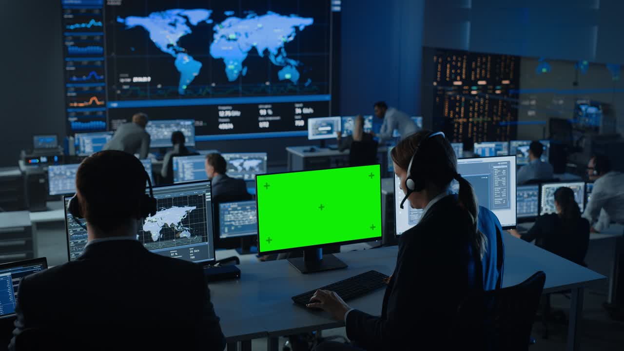 Green Screen Horizontal Mock Up on a Computer Display Used by a Female Technical Client Support Specialist Wearing Headset. Team of Engineers Work in Control and Monitoring Room with Displays with Big Data.