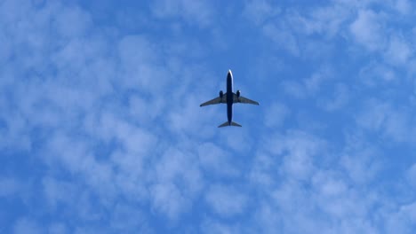 Bottom-up-shot:-Silhouette-of-Airplane-flying-at-blue-sky-between-clouds-in-sunlight---Silhouette-of-aircraft-in-the-air---slow-motion-tracking-shot