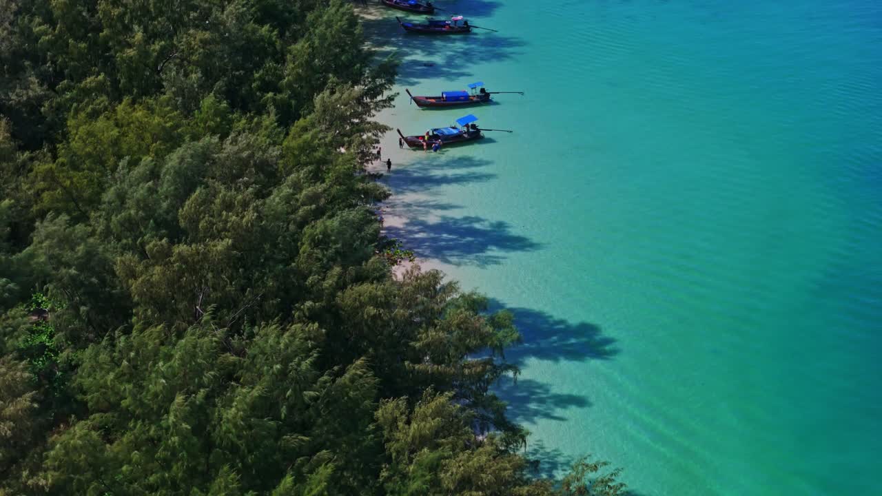Aerial drone shot moving left to right, revealing a pristine tropical beach on Koh Kradan, Thailand, with turquoise waters, lush greenery, white sand, and traditional long-tail boats in 4K.