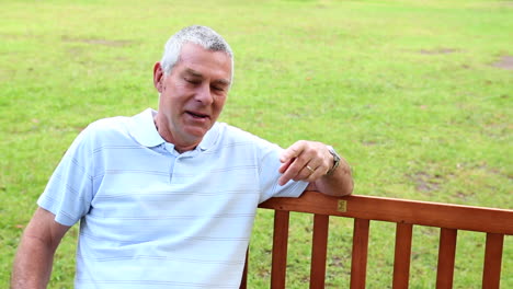 retired man sitting on a park bench talking to the camera