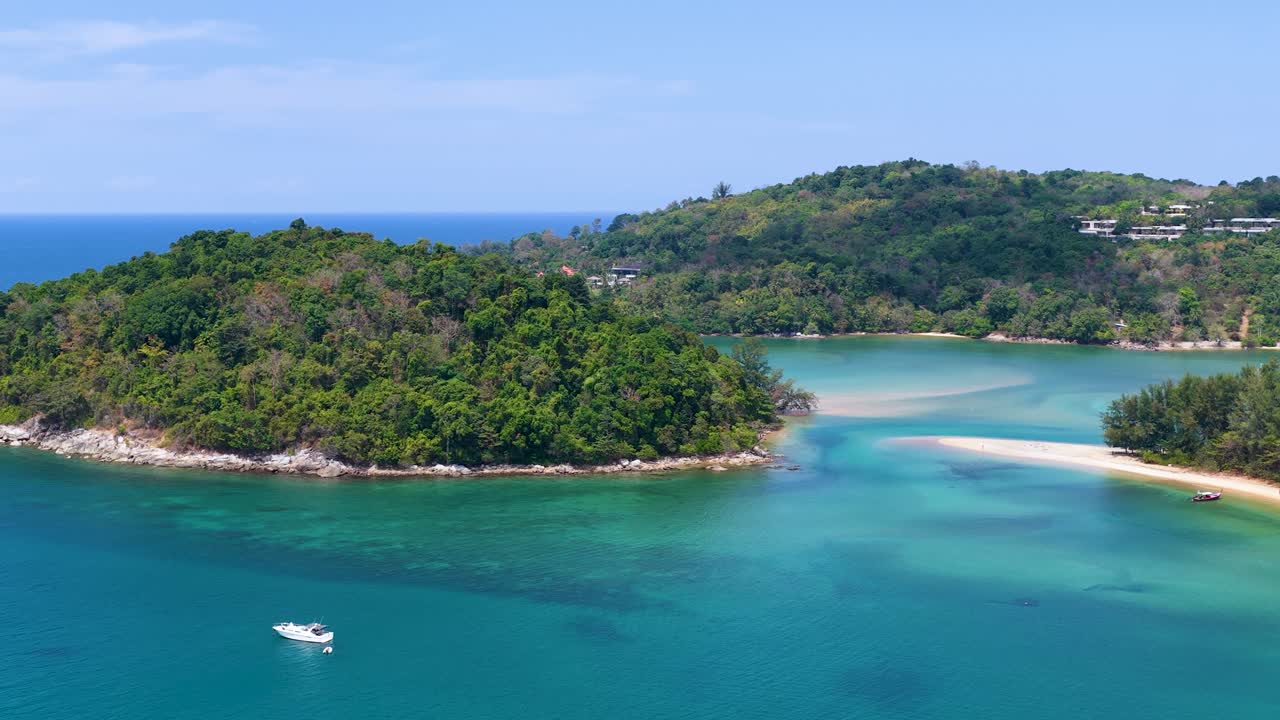Drone footage captures sailboats anchored in clear turquoise water near a lush tropical island