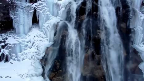 a winter landscape showcases a stunning waterfall partially frozen, surrounded by glistening ice formations and snow. nature's beauty is on full display in this serene location.