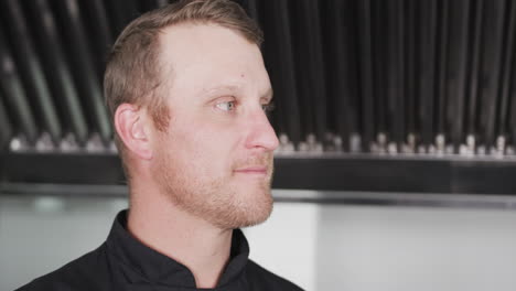 Portrait-of-happy-caucasian-male-chef-turning-and-smiling-in-kitchen,-copy-space,-slow-motion