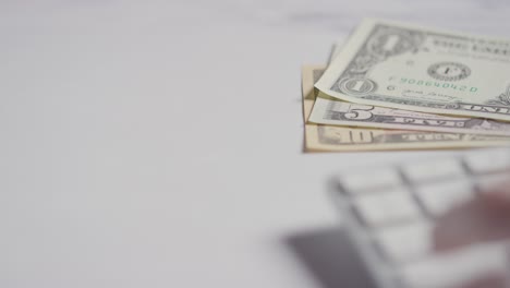 close up currency shot of hand typing on computer keyboard with dollar notes in background