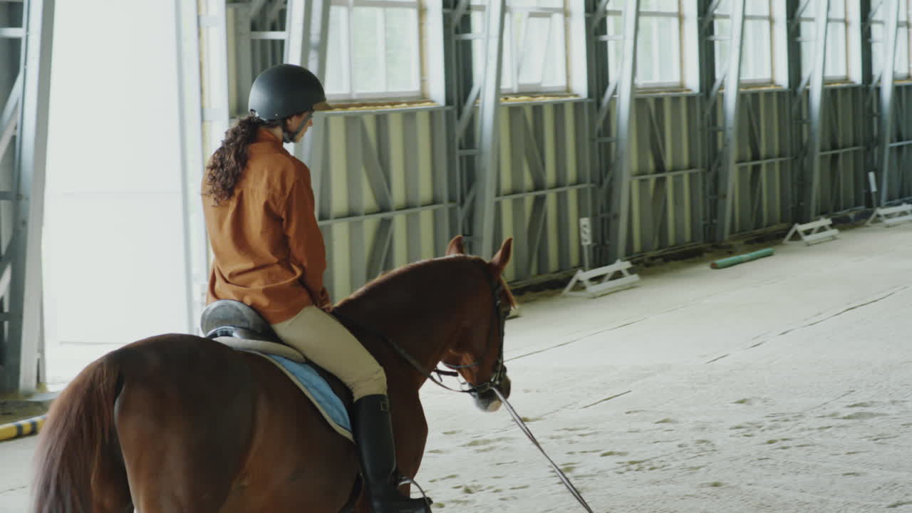 A person riding a horse in an indoor equestrian arena with an instructor