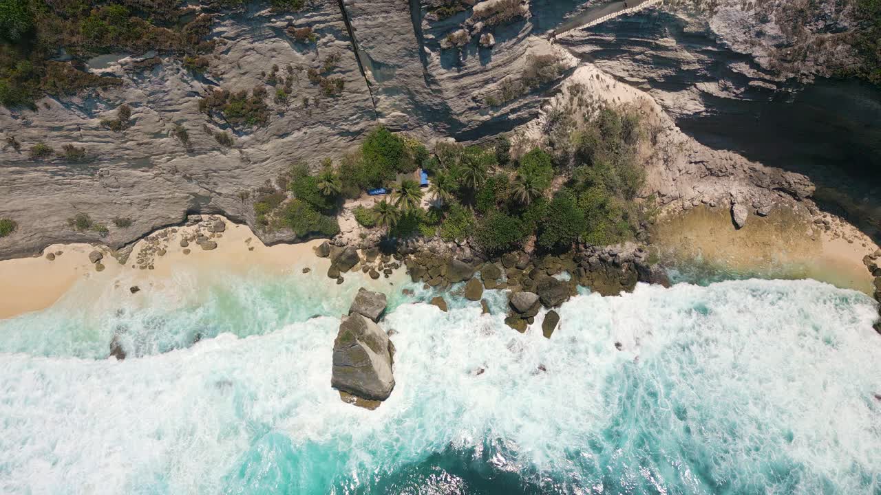 Top down drone view of ocean waves breaking onto a beautiful small sandy beach