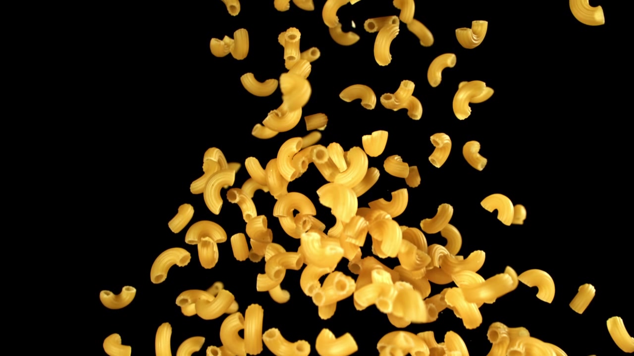 Pasta maccheroni secca che cade al rallentatore su sfondo nero.