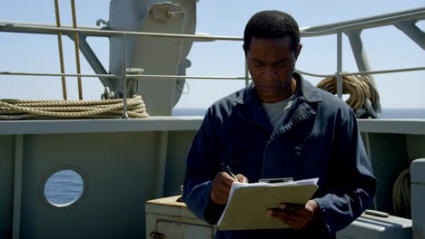 man writes on a clipboard on a ship's deck