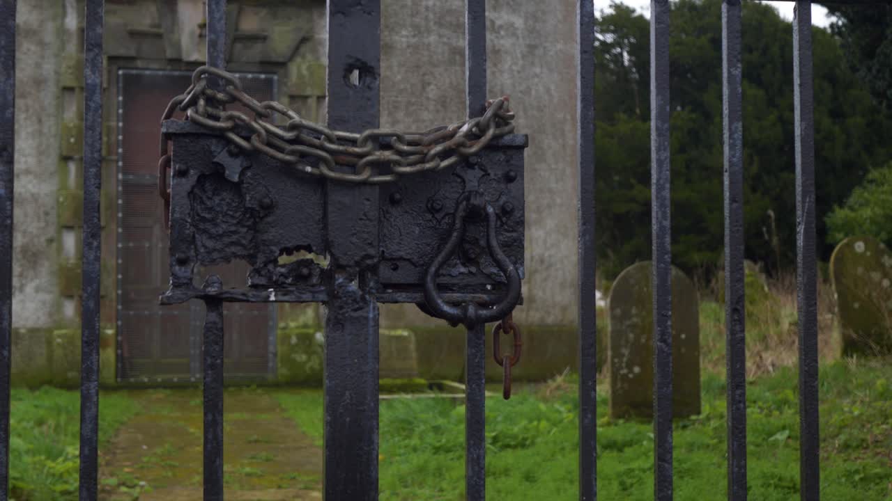una cadena oxidada cierra una puerta de una iglesia abandonada en el condado de cavan, irlanda, un cementerio en el fondo.