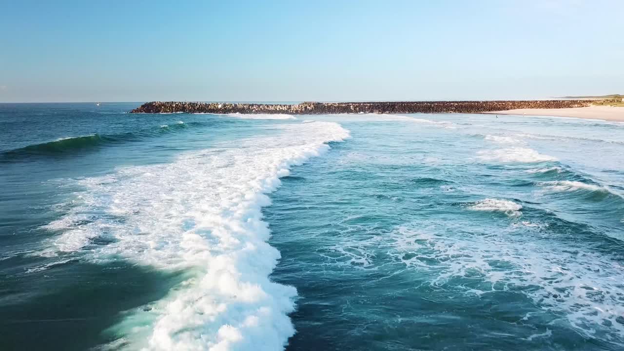 drone volando bajo y paralelo a la playa mientras las olas rompen debajo