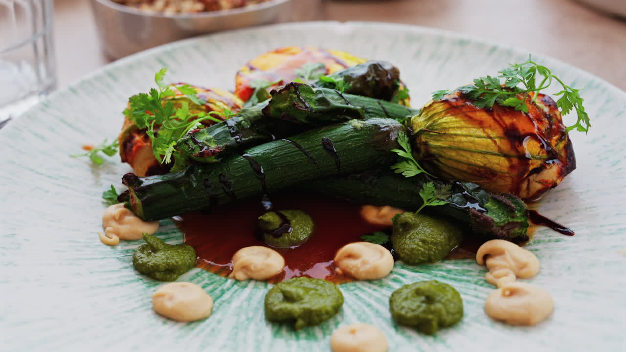 Close up of stuffed zucchini flowers with whole, grilled baby zucchinis on a white plate