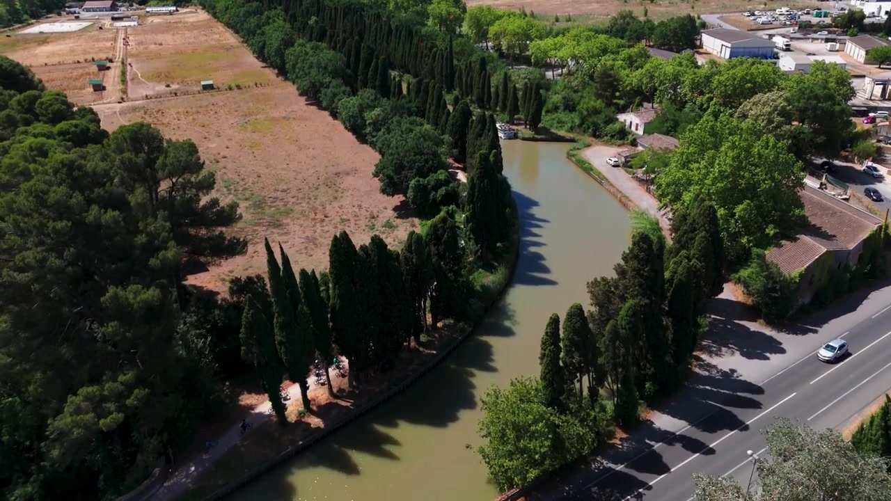 Ripresa aerea con drone che inquadra un canale alberato, l'alzaia e un campo arido in Francia