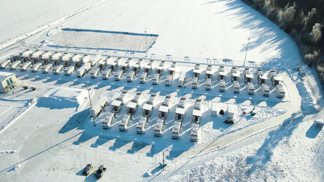 Letecký oblet velkého velkokapacitního zařízení na skladování bateriové energie v Kiise v Estonsku s kontejnerovými skladovacími jednotkami, infrastrukturou elektrické rozvodny a viditelnými pracovníky v zasněžené zimní krajině.