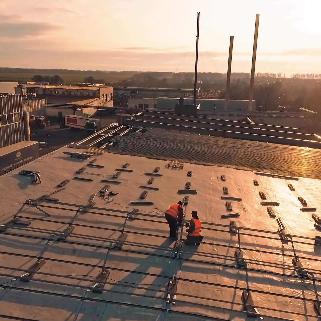 Solar panels installation at sunset. Workers attaching metal basis on roof for sunny batteries on the nature background. Aerial view.
