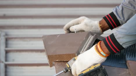 hand with glove using electric drill to screw roof tile, close up