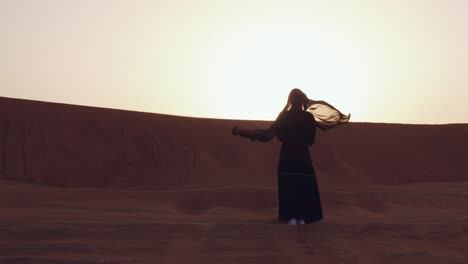 mujer musulmana de pie cerca de la mezquita en el desierto. viento fuerte oriente medio paz sin guerra